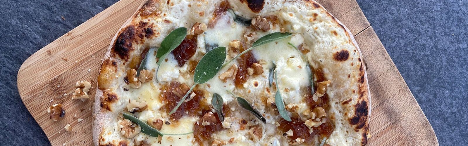Pizza mit aufgeschlagenem Ziegenkäse, Feta, karamellisierten Zwiebeln, Salbei & Walnüssen